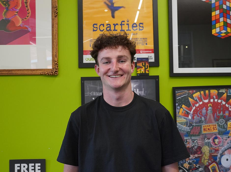 A young man stands in front of a wall of framed OUSA posters.