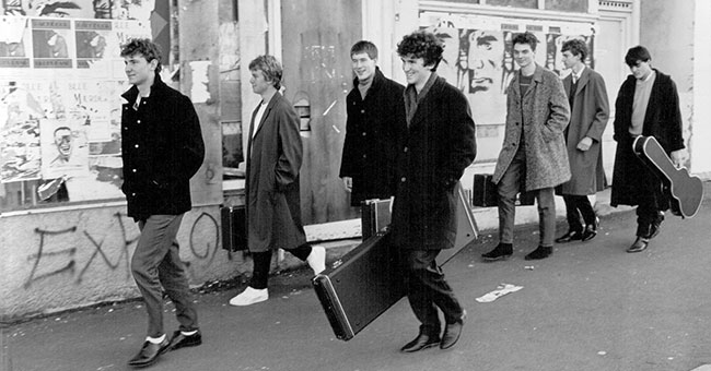 Band members walk along a street in a 1980s photo.