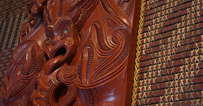 Māori carvings with woven panels on wall in a marae