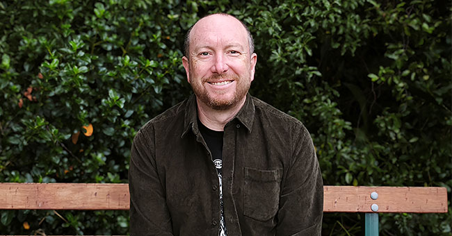 An author picture of Craig Cliff sitting on a park bench outside.