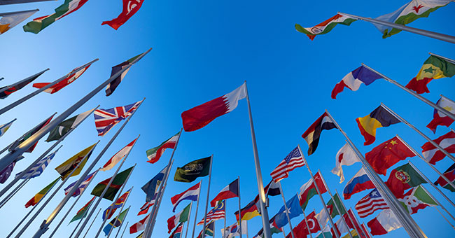 Group of international flags on poles against blue sky image