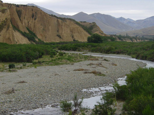 Kyeburn formation in Kyeburn valley. A yellow cliff with deep grooves in it that are tightly spaced. The bedding is sub-horizontal. A river runs through in the foreground.