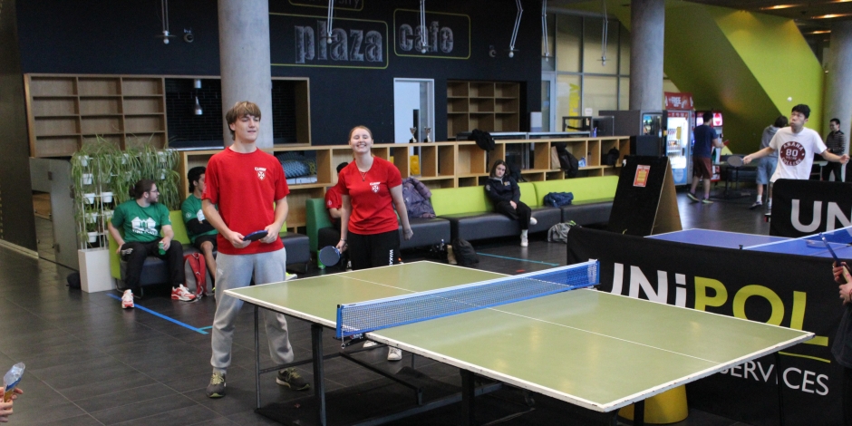 A guy and girl in red t-shirts away the serve in a game of doubles table tennis.