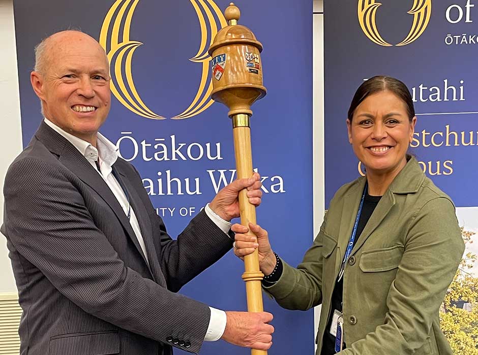 One person handing a large wooden mace to another person 