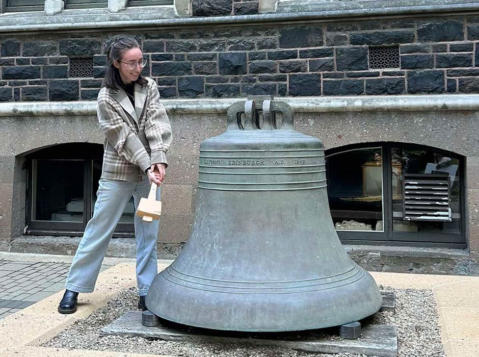 Rebecca Grimwood striking the University bell on the Dunedin campus after submitting her PhD thesis.   