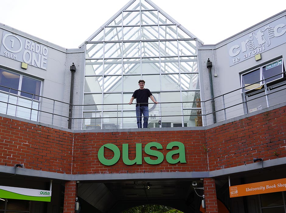 A young man stands above a sign for OUSA.