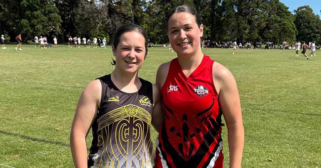 Two women standing on a sunny field wearing sports clothing 