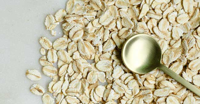 some oats on a smooth white surface with a gold spoon lying on top