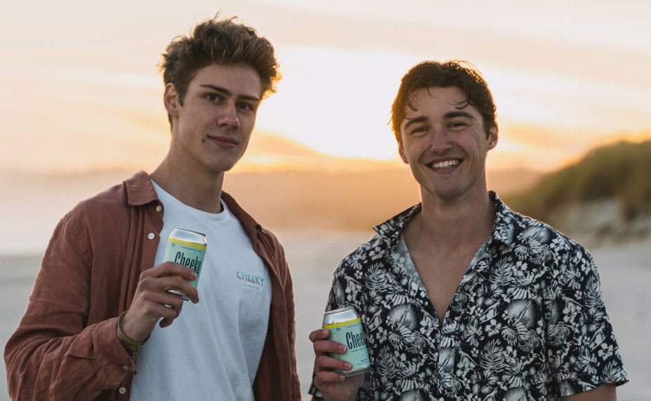 Brendan Yielder and Olivier Despatis holding cans of Cheeky Hard Iced Tea at a beach.