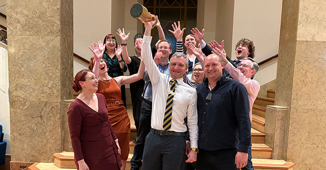 A group of people celebrate as a man holds up a trophy.