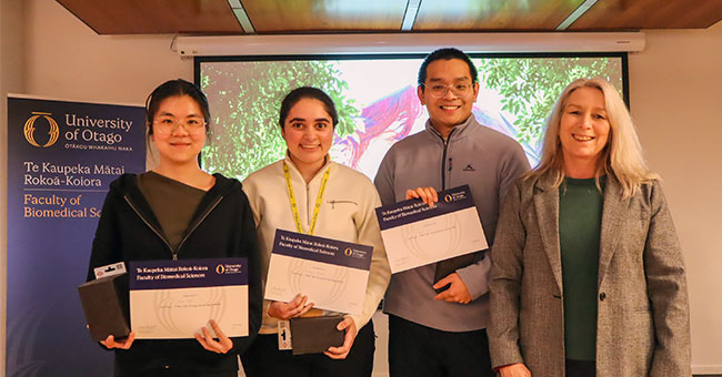 Four people are pictured at a symposium, three with certificates.