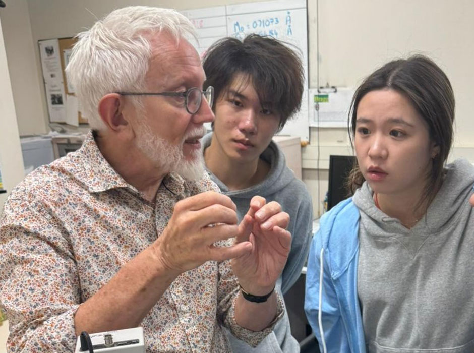 Two people listening to a man speak in a chem lab 
