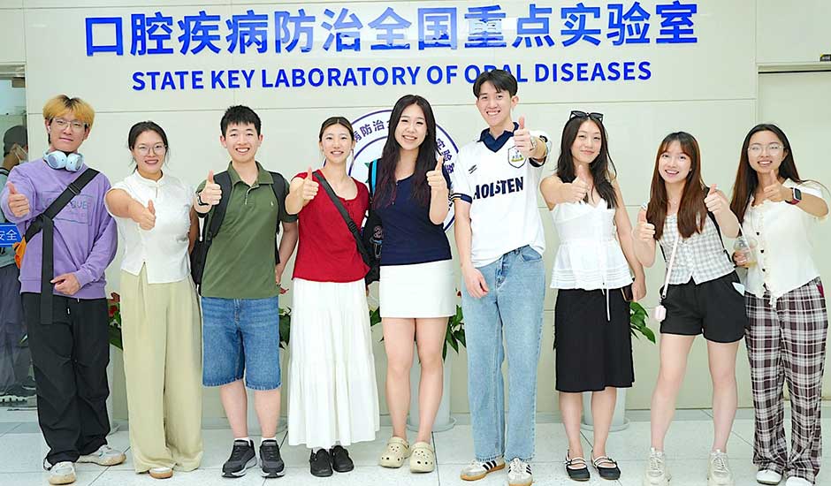 A row of young people standing in front of  a wall with Chinese scripture on it and the words State Key Laboratory of Oral Diseases underneath it