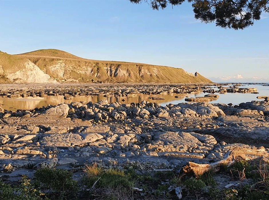 a bay of water with rocks and cliff in the background