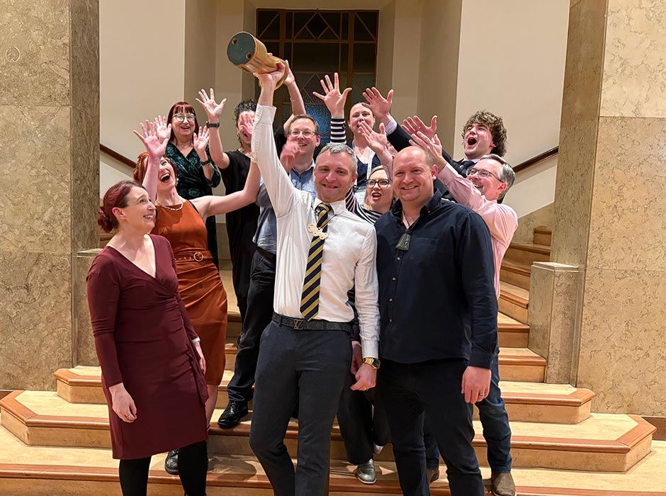 A group of people celebrate as a man holds up a trophy.