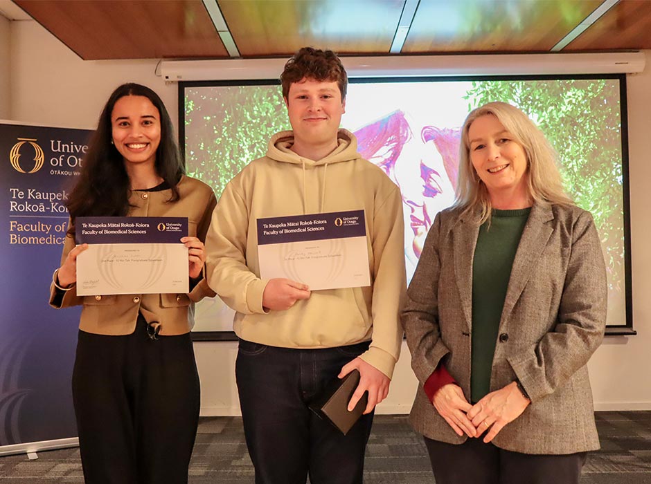 Three people are pictured at a symposium, two holding certificates.
