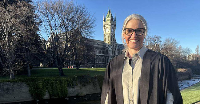 A woman in graduation attire standing in front of the clocktower