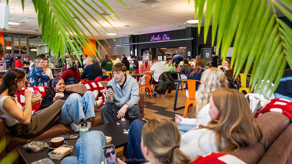 Several groups of students sitting and eating at Auahi Ora cafe, those in the foreground on couches