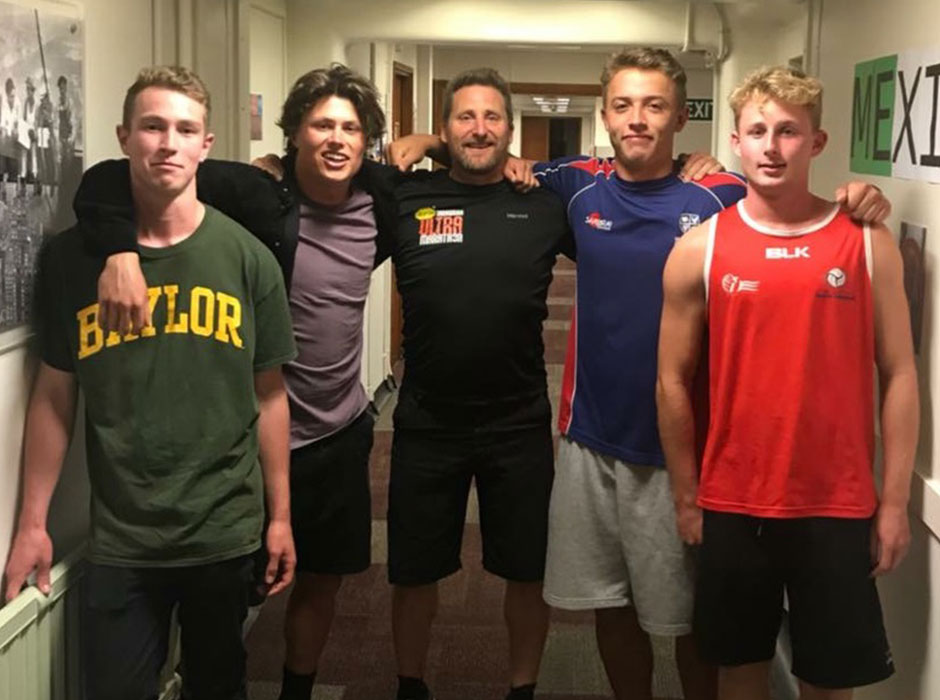 Five men standing next to each other in a college hallway