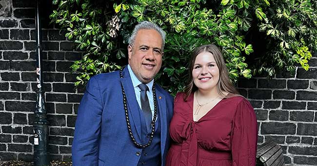 A man and a woman standing in front of a stone wall 