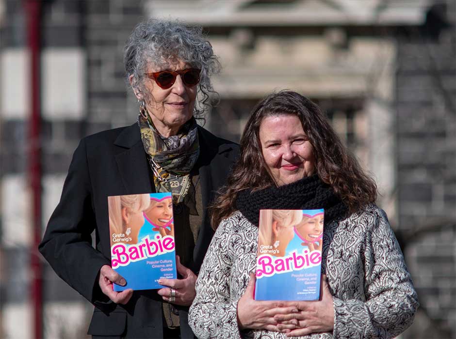 two women standing next to each other, each holding a copy of the Barbie book