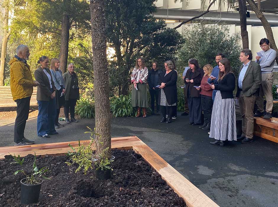 people standing to the side of a raised garden bed singing, some holding sheets of paper