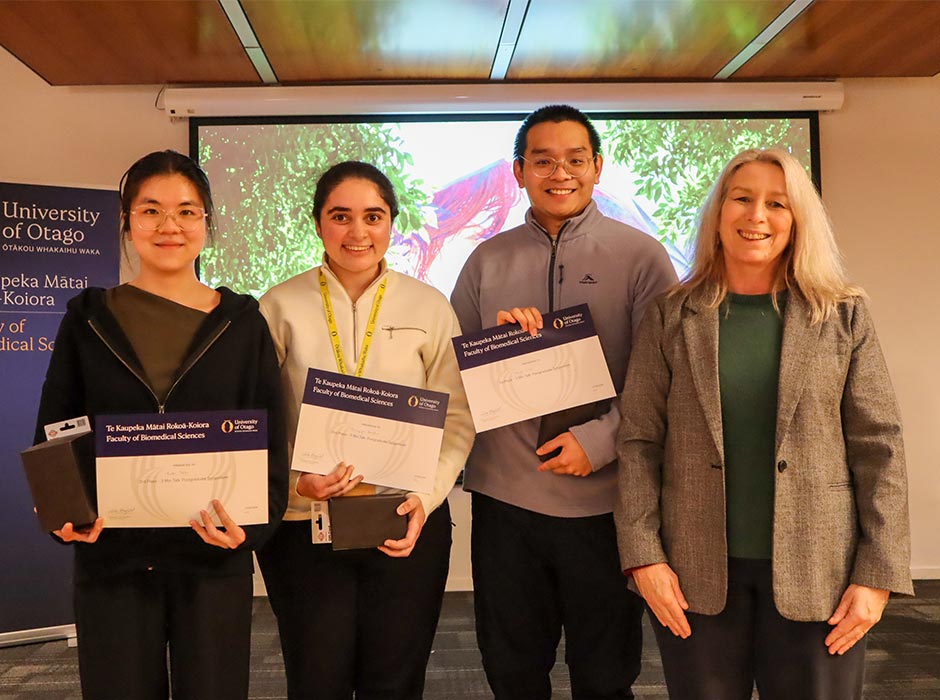 Four people are pictured at a symposium, three with certificates.