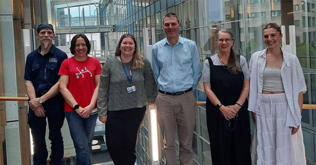 A group of six people pose for a photo in a glass building.