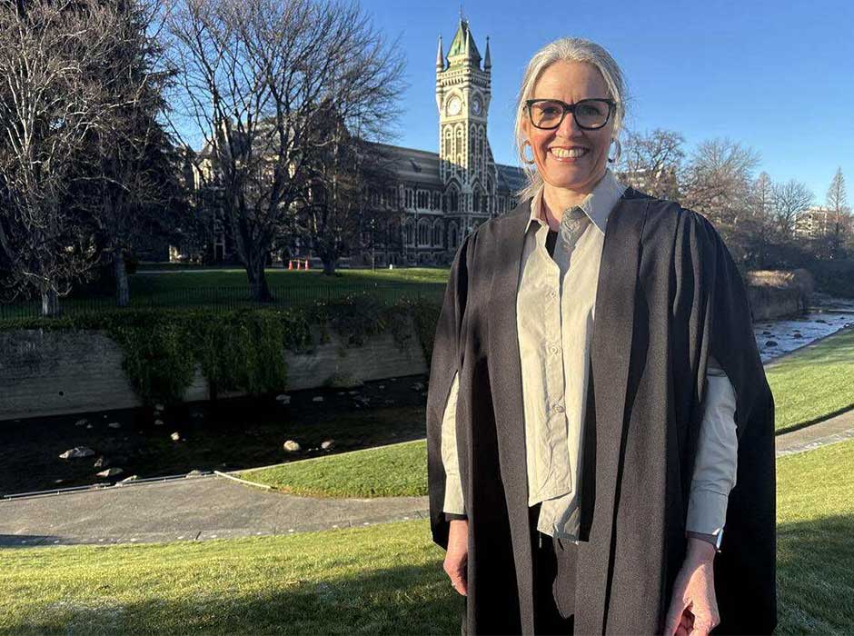 A woman in graduation attire standing in front of the clocktower