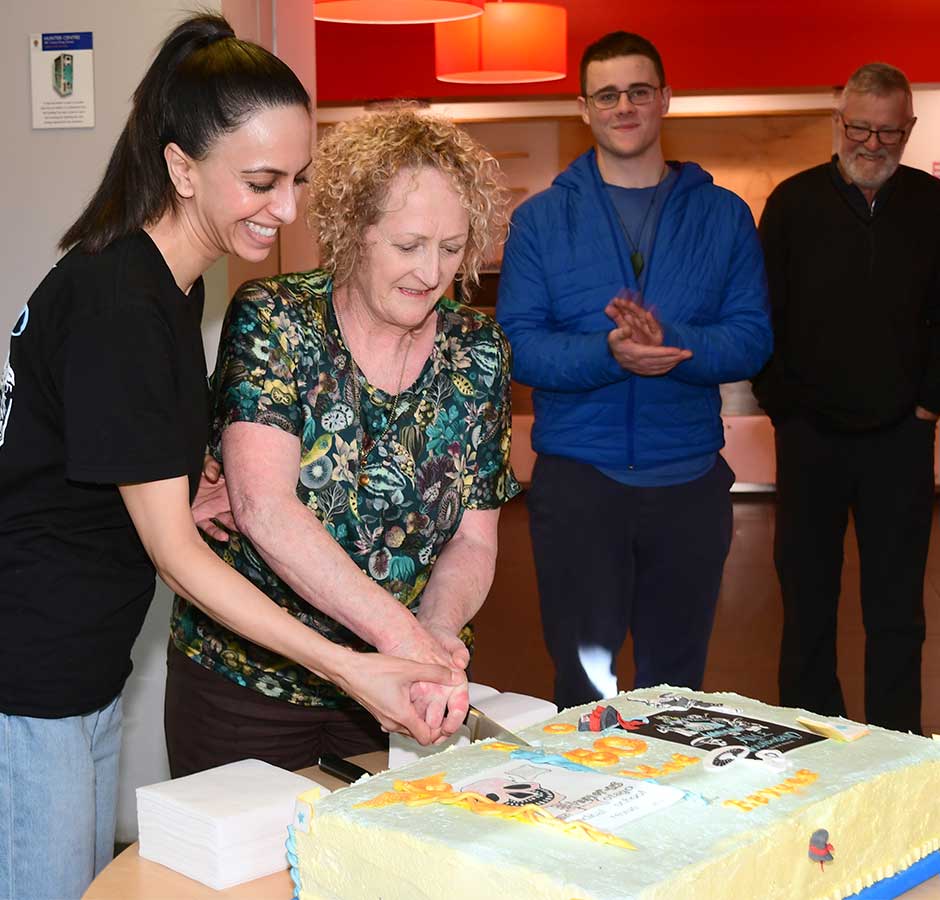 Two women hold a knife together to cut a celebratory cake