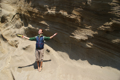 Ben Moorhouse posing in front of a bedded outcrop with arms outstretched