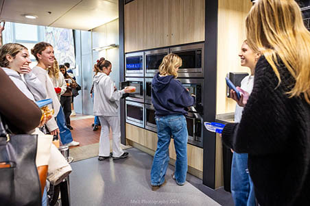 A group of students standing by a wall of microwaves, waiting to heat their food