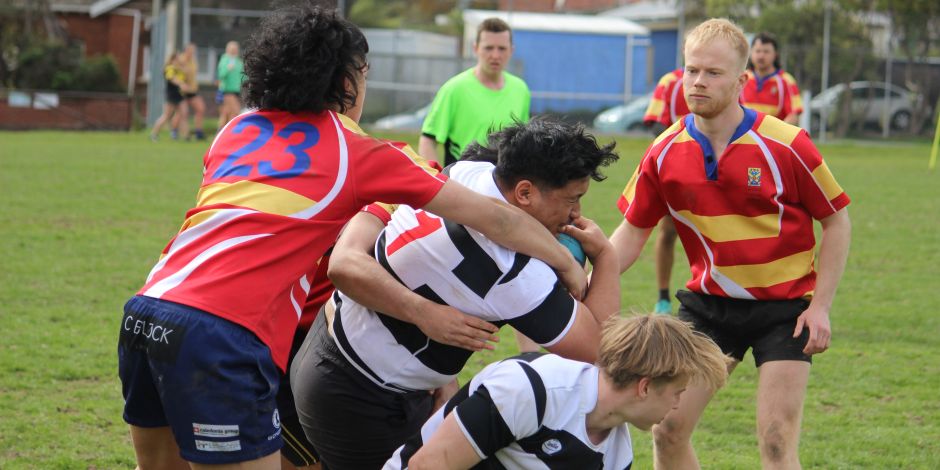 Rugby players from one team tackling a player from the other team who has the ball.