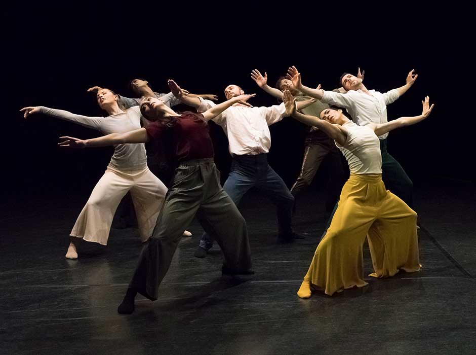 a group of people on stage dancing with their knees slightly bent and their arms open