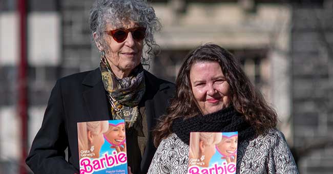 two women standing next to each other, each holding a copy of the Barbie book