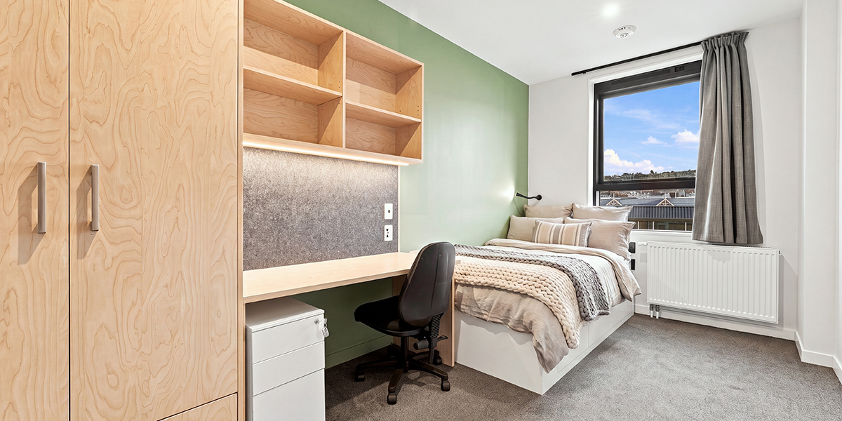 Student bedroom with bed and desk and green feature wall