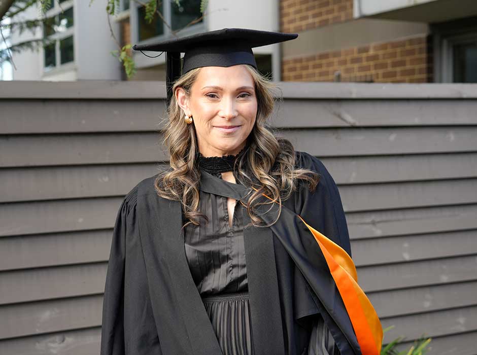 A woman, from waist up, wearing graduation attire in front of a fence