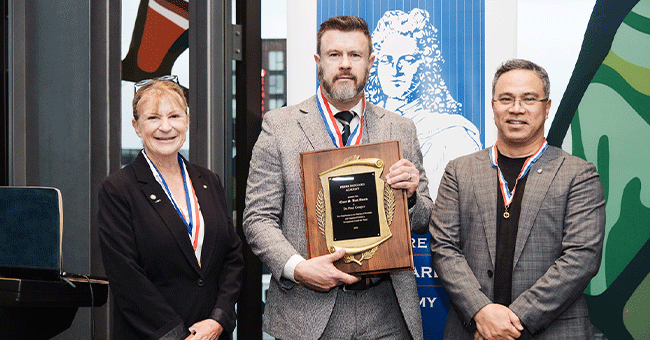 man holding award, with people either side