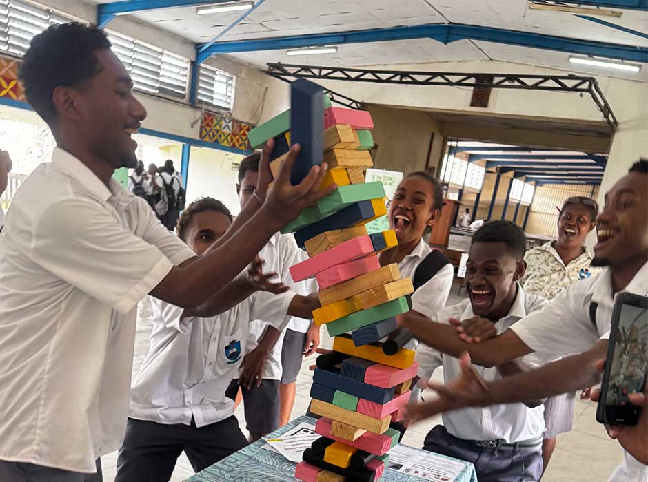 A group of young adults standing around a table, laughing and playing jenga 