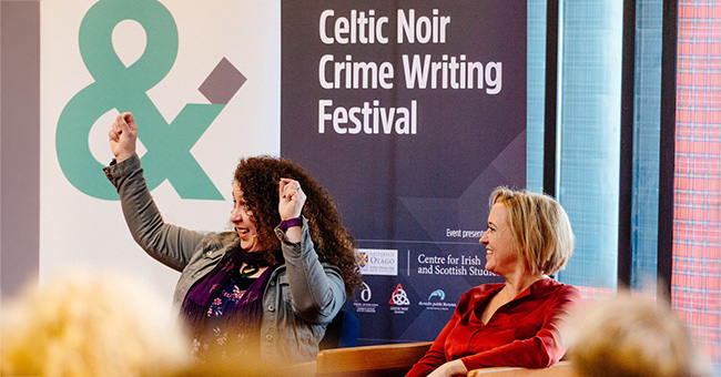 Two women sittug in front of a Celtic Noir Crime Writing Festival sign
