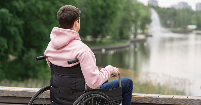 Person in a wheelchair wearing a pink hoodie looking out at a lake