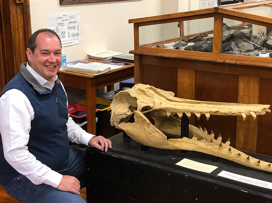 a man sitting next to a large marine mammal fossil