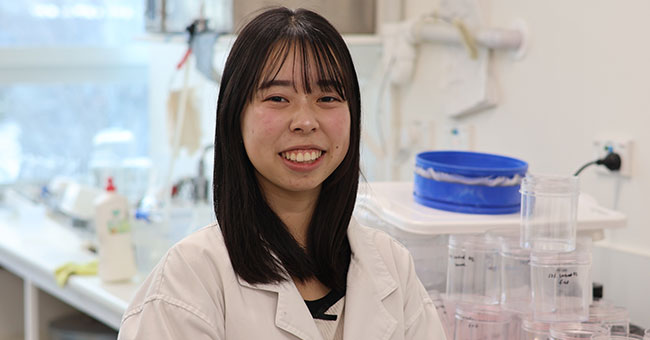 A woman in a science laboratory faces the camera smiling.