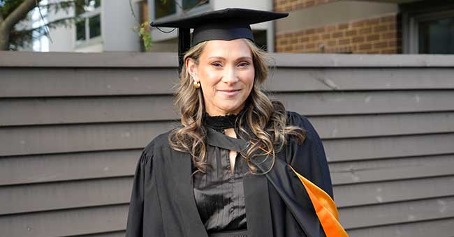 A woman, from waist up, wearing graduation attire in front of a fence