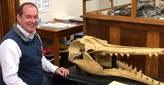 a man sitting next to a large marine mammal fossil