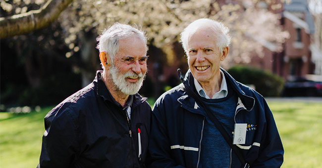 Two men pictured smiling outdoors.