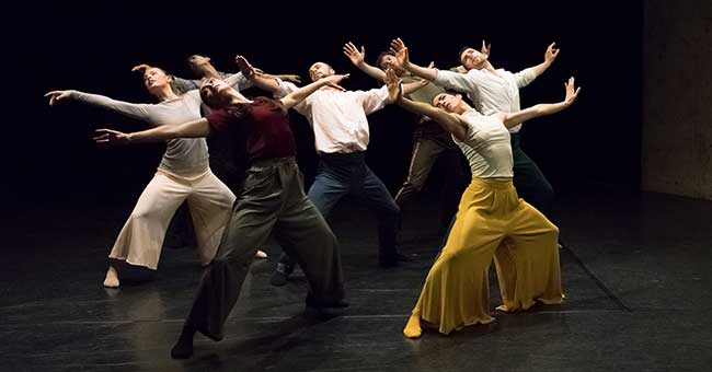 a group of people on stage dancing with their knees slightly bent and their arms open 
