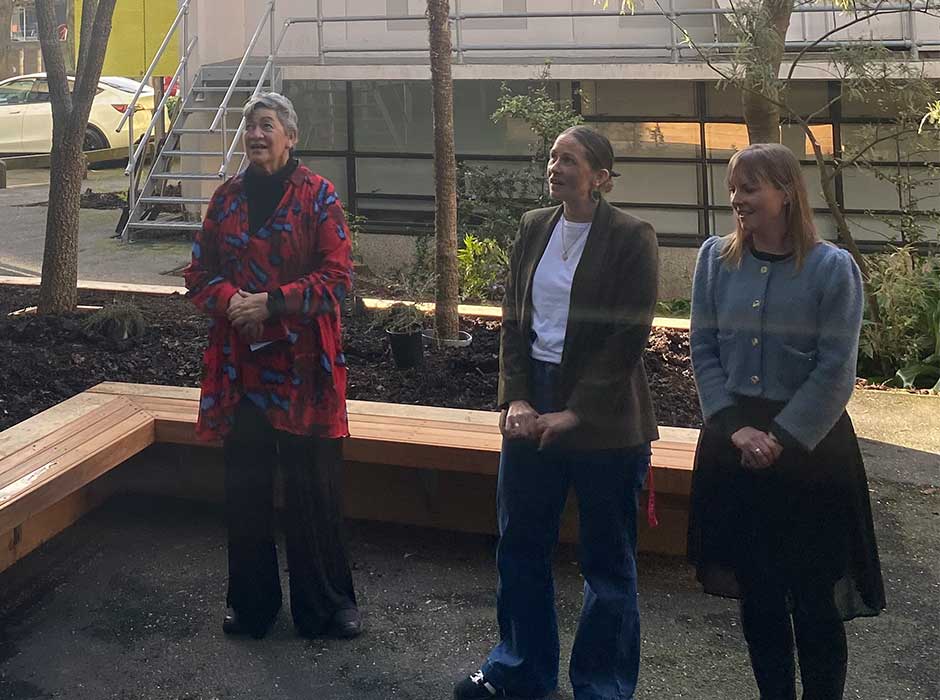 three women standing singing in front of a newly made raised garden bed