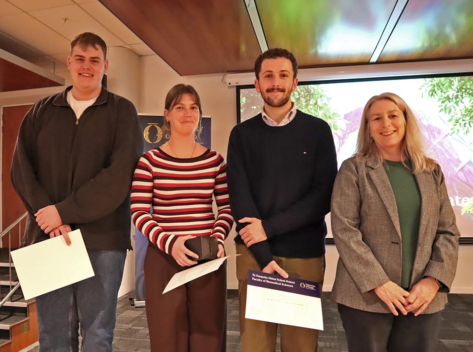Four people are pictured at a symposium, three with certificates.