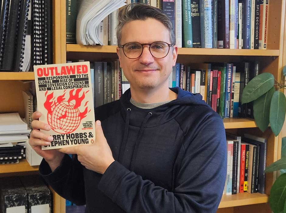 A man standing in front of a bookcase holding up a book